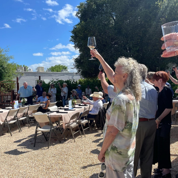 People standing around tables and chairs holding glasses in the air