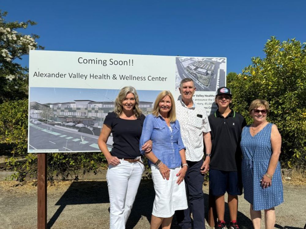 five people smiling standing together in front of Alexander Valley Health and Wellness Center "Coming Soon" sign