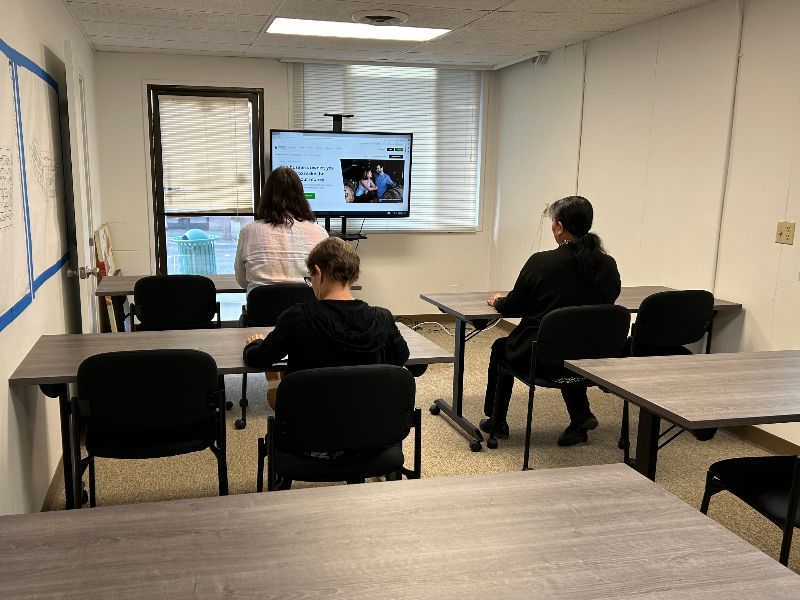 People sitting at tables facing away from camera looking at screen in an office