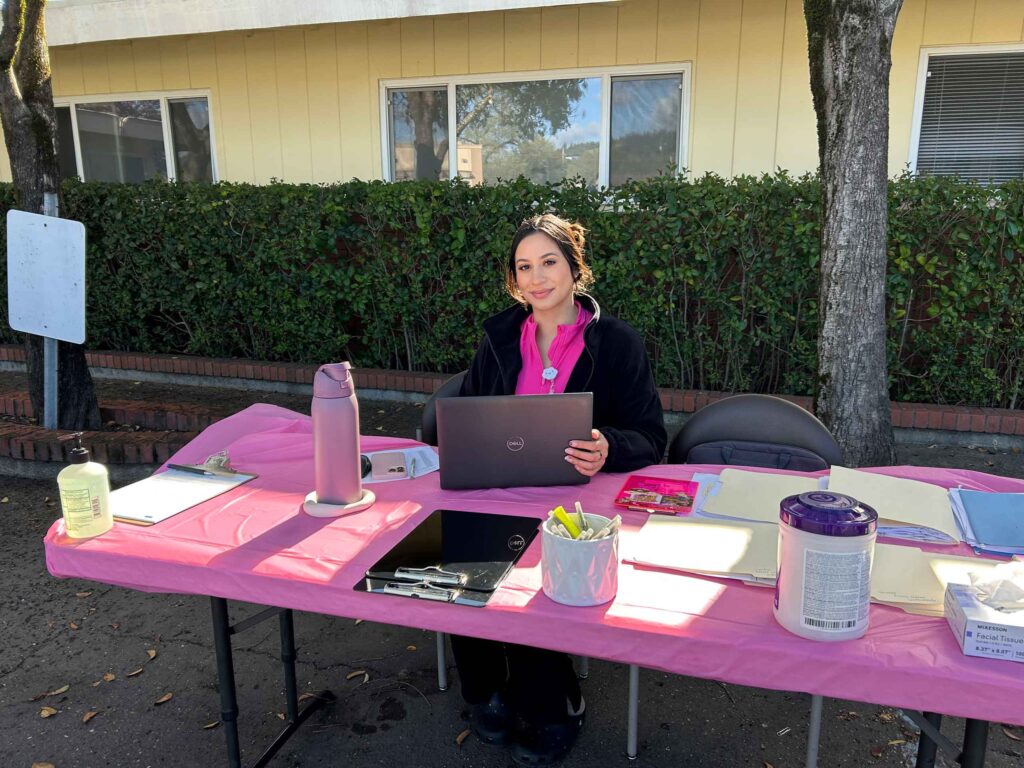young woman at a health table with pink clothes and tablecloth